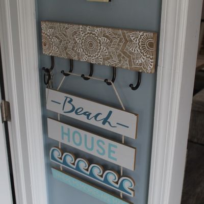 Sale Photo Thumbnail #32: Carved wood wall-mounted key rack with metal hooks, mounted above a hanging decorative beach house wooden sign.