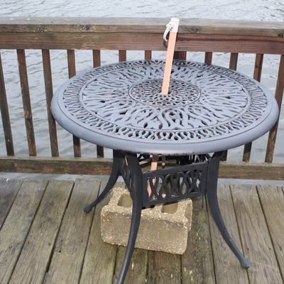 Sale Photo Thumbnail #58: Round cast aluminum outdoor patio bistro table featuring an ornate filigree top and umbrella hole, set on a wooden deck.