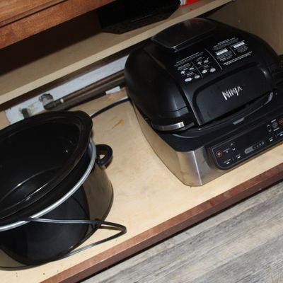 Sale Photo Thumbnail #4: Ninja Foodi indoor grill and a black Crock-Pot slow cooker, stored inside a wooden lower kitchen cabinet.