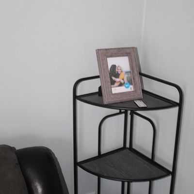 Sale Photo Thumbnail #23: Modern 3-tier corner shelf unit with black metal frame and grey wood-grain shelves, topped with a picture frame.