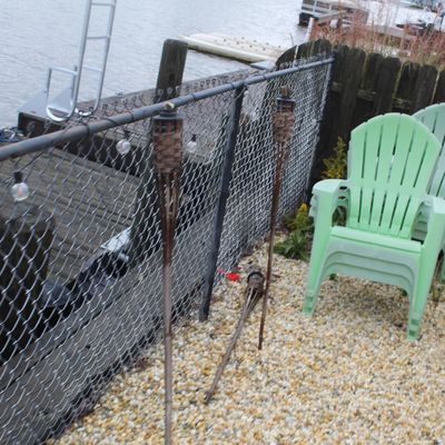 Sale Photo Thumbnail #59: Stackable light green plastic Adirondack-style lawn chairs, tiki torches, and string lights arranged along a chain-link dock fence.
