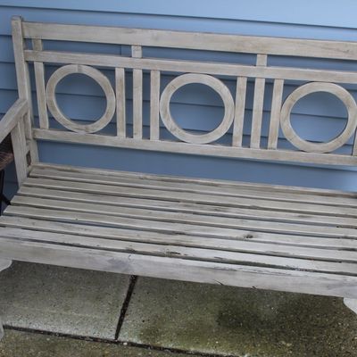 Sale Photo Thumbnail #67: Weathered wooden garden bench with a slatted seat and circle-motif backrest, accompanied by a small dark wicker side table.