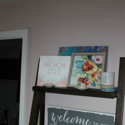 Sale Photo Thumbnail #6: Selection of modern coastal wall decor and framed floral art displayed on a dark wood ladder shelf alongside small decorative accessories.