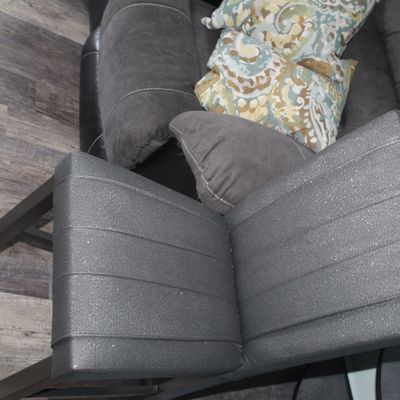 Sale Photo Thumbnail #21: Modern charcoal grey bar stool with channeled faux leather upholstery and a dark wooden frame, shown near a reclining couch with patterned throw pillows.