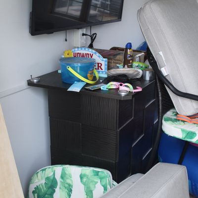 Sale Photo Thumbnail #62: A modern black accent cabinet holding assorted pool items, alongside a patio chair with cushions and a wall-mounted flat-screen television.