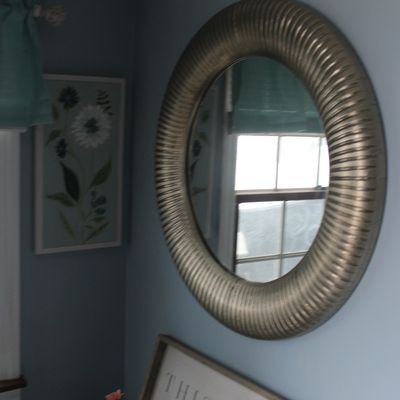Sale Photo Thumbnail #31: Large round wall mirror featuring a ribbed metallic pewter frame, displayed on a light blue wall alongside framed wall art.