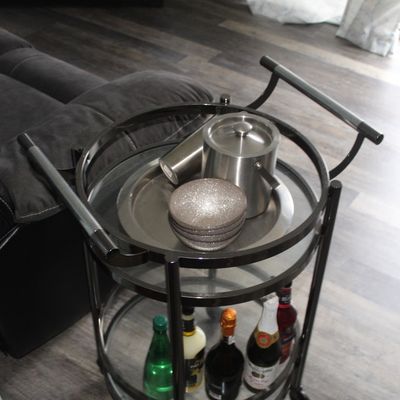 Sale Photo Thumbnail #20: Modern round black metal bar cart with glass tiers, featuring bar accessories and bottled beverages.