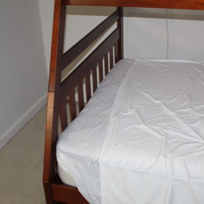 Sale Photo Thumbnail #81: Modern cherry-finished wooden bunk bed frame with a mattress dressed in a white sheet.