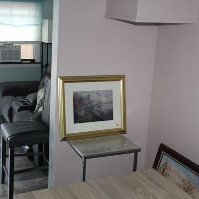Sale Photo Thumbnail #18: Framed hot air balloon landscape art print displayed on a small metallic side table in a room with additional framed artwork.