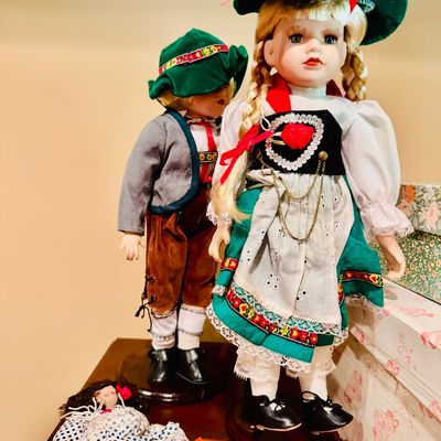 Sale Photo Thumbnail #61: Pair of vintage collectible porcelain dolls in traditional Alpine folk attire, displayed alongside souvenir castanets and a small doll in a polka-dot dress.