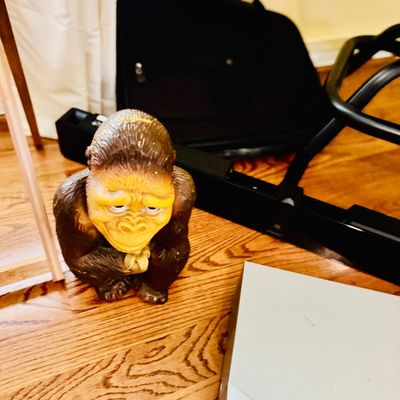 Sale Photo Thumbnail #74: Vintage molded plastic gorilla coin bank with a light yellow face and brown fur texture, sitting on a hardwood floor.