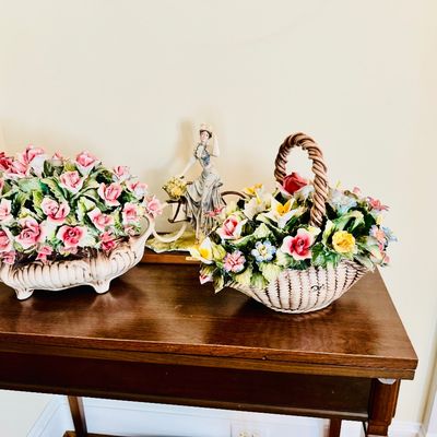 Sale Photo Thumbnail #8: Collection of vintage Capodimonte-style porcelain floral arrangements, including two woven basket displays filled with colorful flowers and a figurine of a woman on a bicycle.