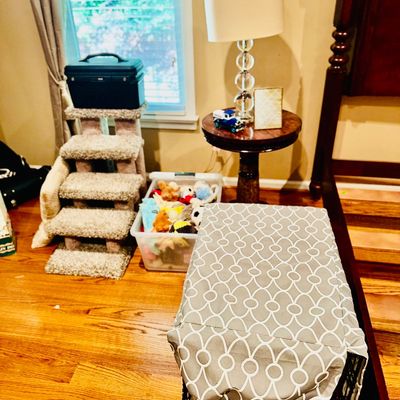 Sale Photo Thumbnail #65: Pet supply assortment including a covered wire crate, carpeted pet stairs, a clear storage bin filled with stuffed toys, and a round pedestal end table with a modern stack-ball table lamp.