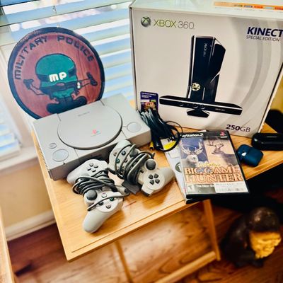 Sale Photo Thumbnail #75: Collection of gaming items featuring an original Sony PlayStation console with controllers, a boxed Xbox 360 Kinect Special Edition set, PlayStation 2 games, and a Military Police plaque.