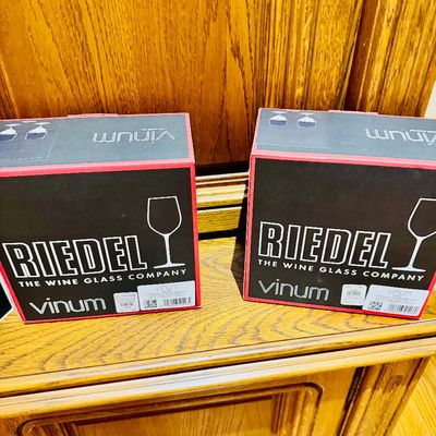 Sale Photo Thumbnail #15: Two boxed sets of Riedel Vinum series crystal wine glasses resting on a wooden cabinet shelf.