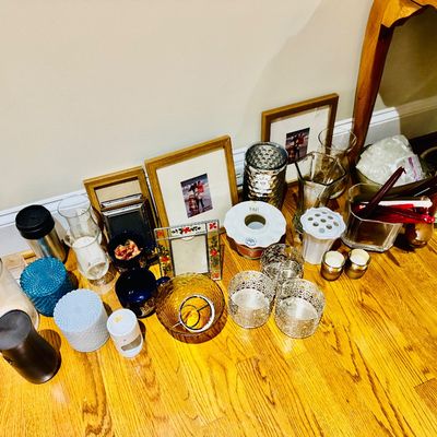 Sale Photo Thumbnail #25: Collection of home decor items including picture frames, glass vases, candle holders, textured jars, and mugs arranged on a hardwood floor.