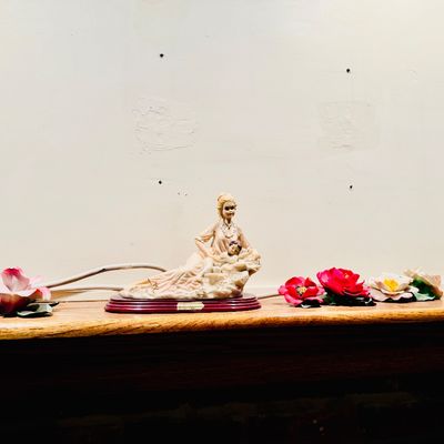 Sale Photo Thumbnail #23: Vintage Giuseppe Armani resin figurine of a mother with child on a wooden base, displayed alongside decorative porcelain flower accents on a mantle.