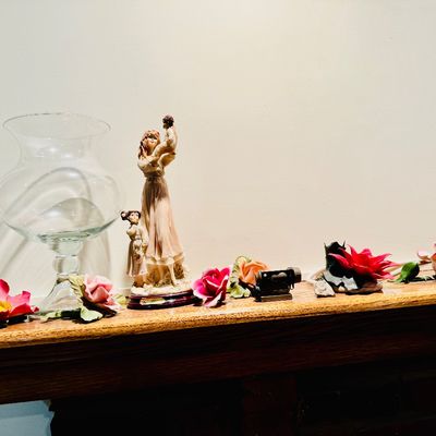 Sale Photo Thumbnail #22: Collection of decorative mantel items including a clear glass hurricane vase, resin mother-and-child figurine, and various ceramic floral accents.