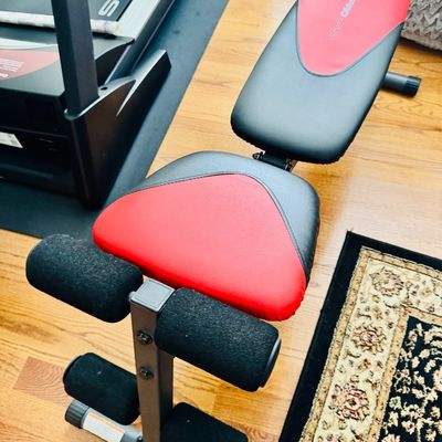 Sale Photo Thumbnail #43: Weider Pro 255 L adjustable weight bench with red and black vinyl padding and foam leg rollers, positioned next to a Sole treadmill.
