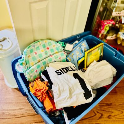 Sale Photo Thumbnail #78: Blue plastic storage tote filled with assorted children's items, including folded clothing, a small patterned backpack, and gift bags.