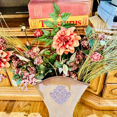 Sale Photo Thumbnail #17: Faux floral arrangement in a flared metal vase with a filigree motif, displayed in front of reference books.