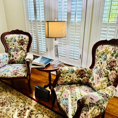 Sale Photo Thumbnail #5: Pair of traditional carved wood armchair featuring floral tapestry upholstery, flanking a small round accent table with a crystal base lamp.
