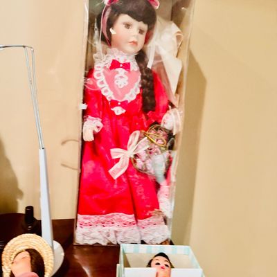 Sale Photo Thumbnail #59: Vintage porcelain doll in a red and white lace dress, preserved inside its original box alongside other boxed dolls.
