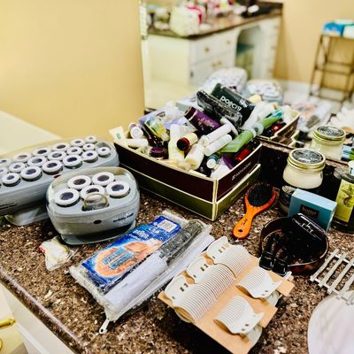 Sale Photo Thumbnail #69: Collection of vintage and modern personal care items, including BaByliss electric hot rollers, hair clips, brushes, and various cosmetic travel bottles arranged on a granite bathroom vanity.