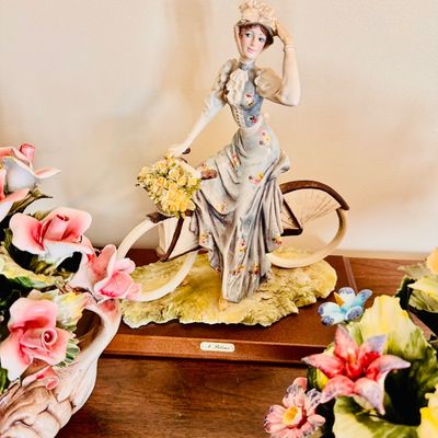 Sale Photo Thumbnail #7: Vintage Capodimonte-style porcelain figurine depicting a woman in Victorian attire posing on a bicycle with a basket of flowers, mounted on a wooden base.