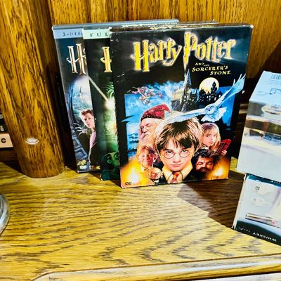 Sale Photo Thumbnail #13: Collection of three early 2000s Harry Potter DVD sets displayed on a wooden shelf, including Harry Potter and the Sorcerer's Stone.