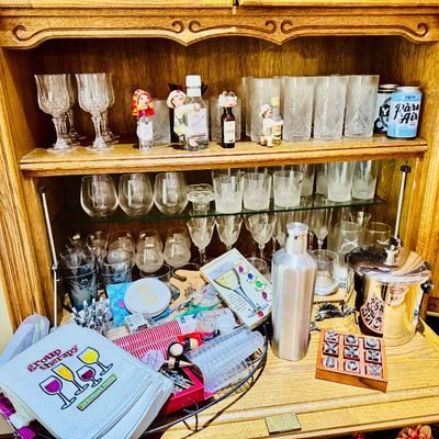 Sale Photo Thumbnail #18: Oak hutch filled with assorted glassware including wine goblets and tumblers, alongside barware accessories, a stainless steel cocktail shaker, and a silver-tone ice bucket.