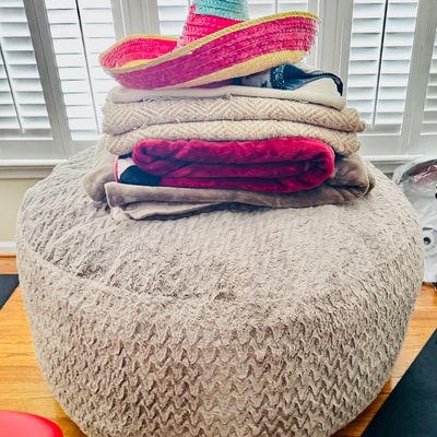 Sale Photo Thumbnail #44: Large beige plush ottoman topped with a stack of folded blankets and a colorful straw sombrero.