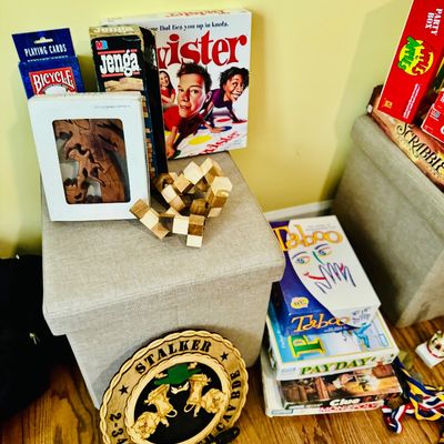 Sale Photo Thumbnail #77: Collection of classic board games and puzzles, including Twister, Jenga, Taboo, PayDay, and wooden brain teasers, displayed alongside a military plaque.