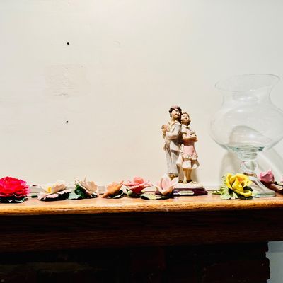 Sale Photo Thumbnail #24: Collection of decorative porcelain floral pieces, a couple figurine, and a clear glass hurricane vase, displayed on a wooden mantle.