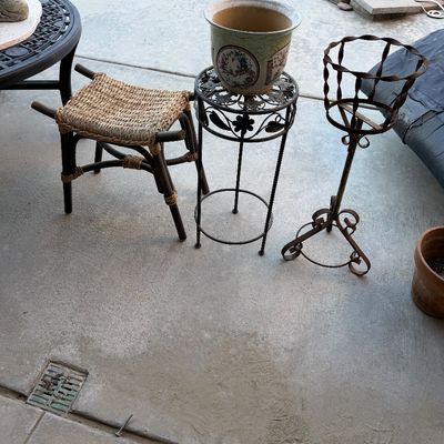 Collection of patio decor including a woven rush-seat footstool, wrought iron plant stands, and a large decorated ceramic planter.