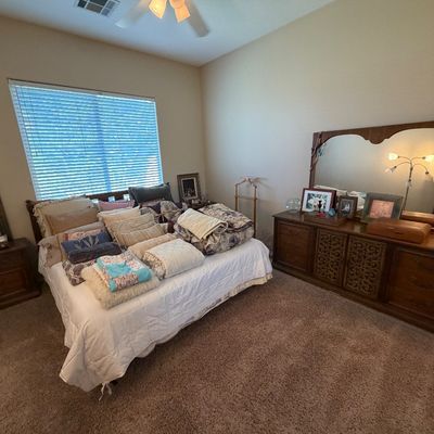 Bedroom suite including a bed covered in folded quilts and decorative pillows, a nightstand, and a dark wood long dresser with matching...