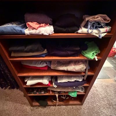Tall dark wood bookcase filled with stacks of neatly folded assorted clothing and linens.