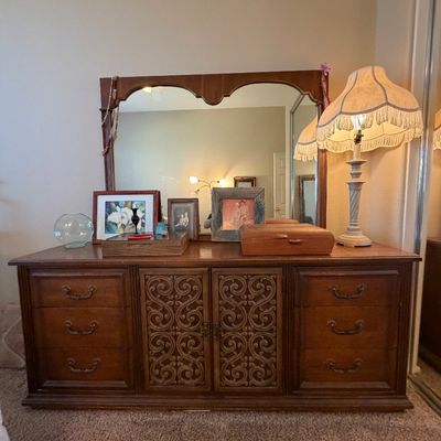 Vintage dark wood triple dresser with carved scrollwork cabinet doors, matching attached mirror, and various tabletop decor including a...