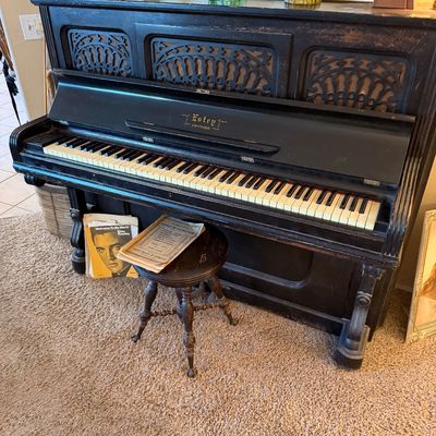 Vintage black Estey upright piano with carved fretwork panels, complete with a swivel stool and vintage sheet music.