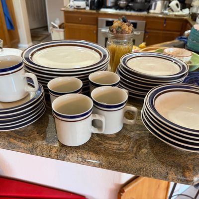 Vintage stoneware dinnerware set featuring a cream base with blue and brown striped rim accents, including plates, bowls, cups, and saucers.