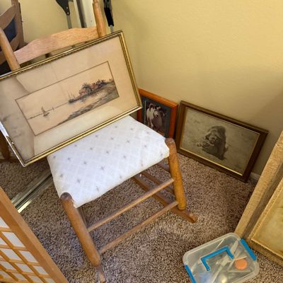 Vintage wooden child's rocking chair with an upholstered seat, displaying a framed landscape watercolor print alongside other framed...