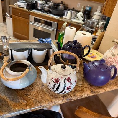 Collection of ceramic teapots, including Japanese-style handles and solid purple glazes, displayed alongside a floral porcelain pitcher...