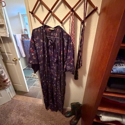Vintage dark floral kimono-style robe and pattern scarves hanging from an expandable wooden accordion wall rack.