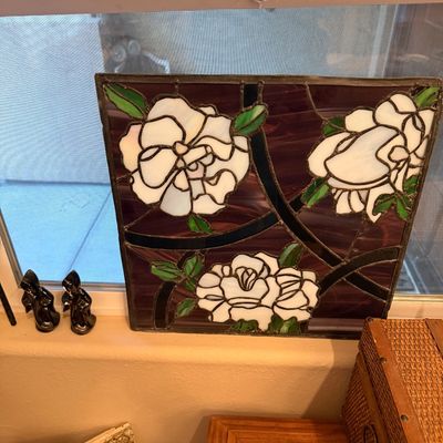 Square stained glass window panel featuring white flowers and green leaves set against dark plum and black slag glass background.