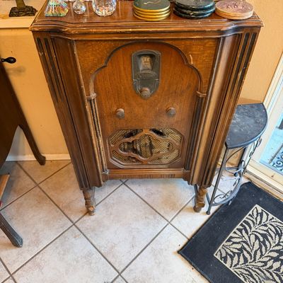 Vintage Majestic floor-standing console radio in a carved wooden cabinet with surface wear, displayed with decorative smalls and coasters...