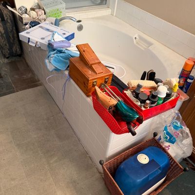 A collection of household and personal care items arranged around a bathtub, including a wooden shoe shine box, shoe stretchers, shoe...