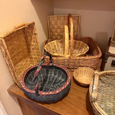 Collection of assortment woven baskets in various shapes, sizes, and natural wood tones, including a navy and red painted handle basket.