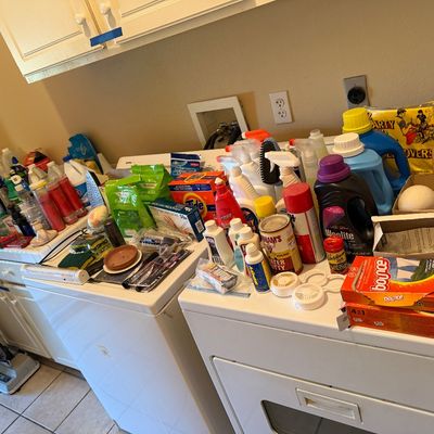 Large assortment of household cleaning supplies, laundry detergents, and utility items arranged on washing machines and countertops.