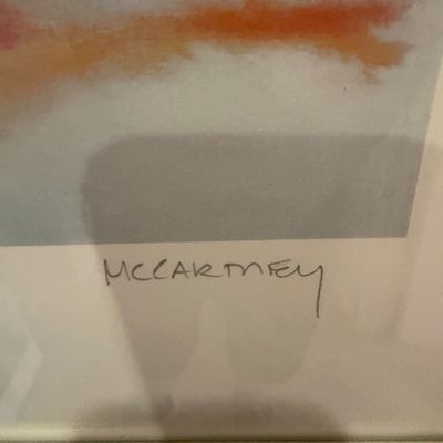 Close-up detail of a signature reading "MCCARTNEY" on a framed artwork with orange and neutral tones.