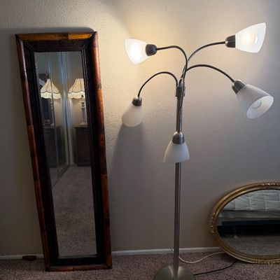 Brushed metal modern multi-arm floor lamp with frosted white glass shades, displayed alongside a faux bamboo floor mirror and a gold oval...